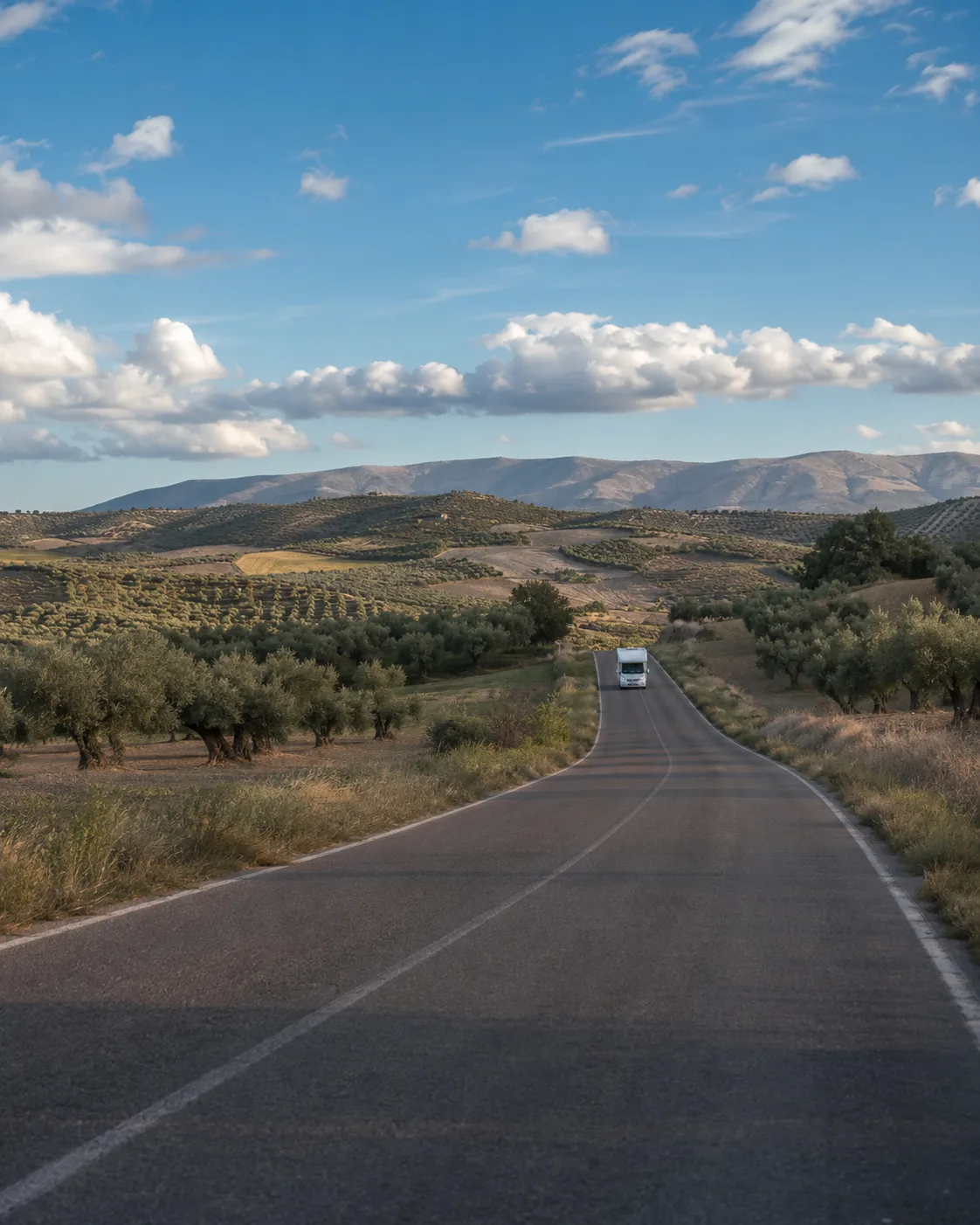 Autocaravana viajando por una carretera secundaria entre campos al atardecer